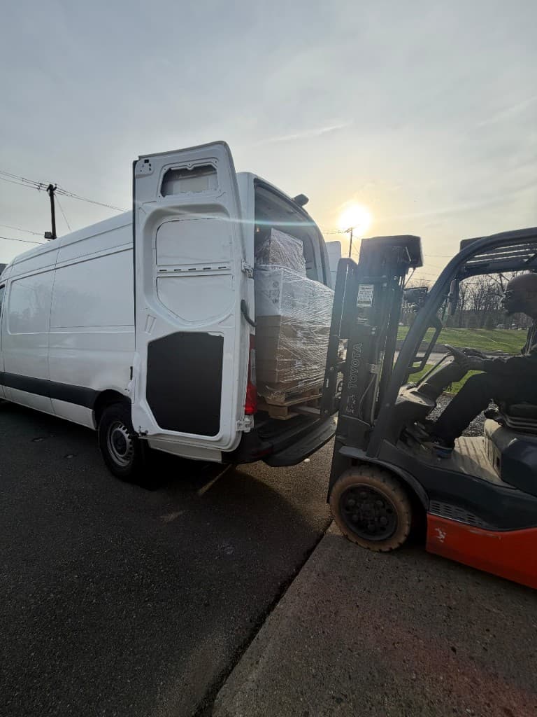 White cargo van and forklift loading palletized freight at a distribution yard